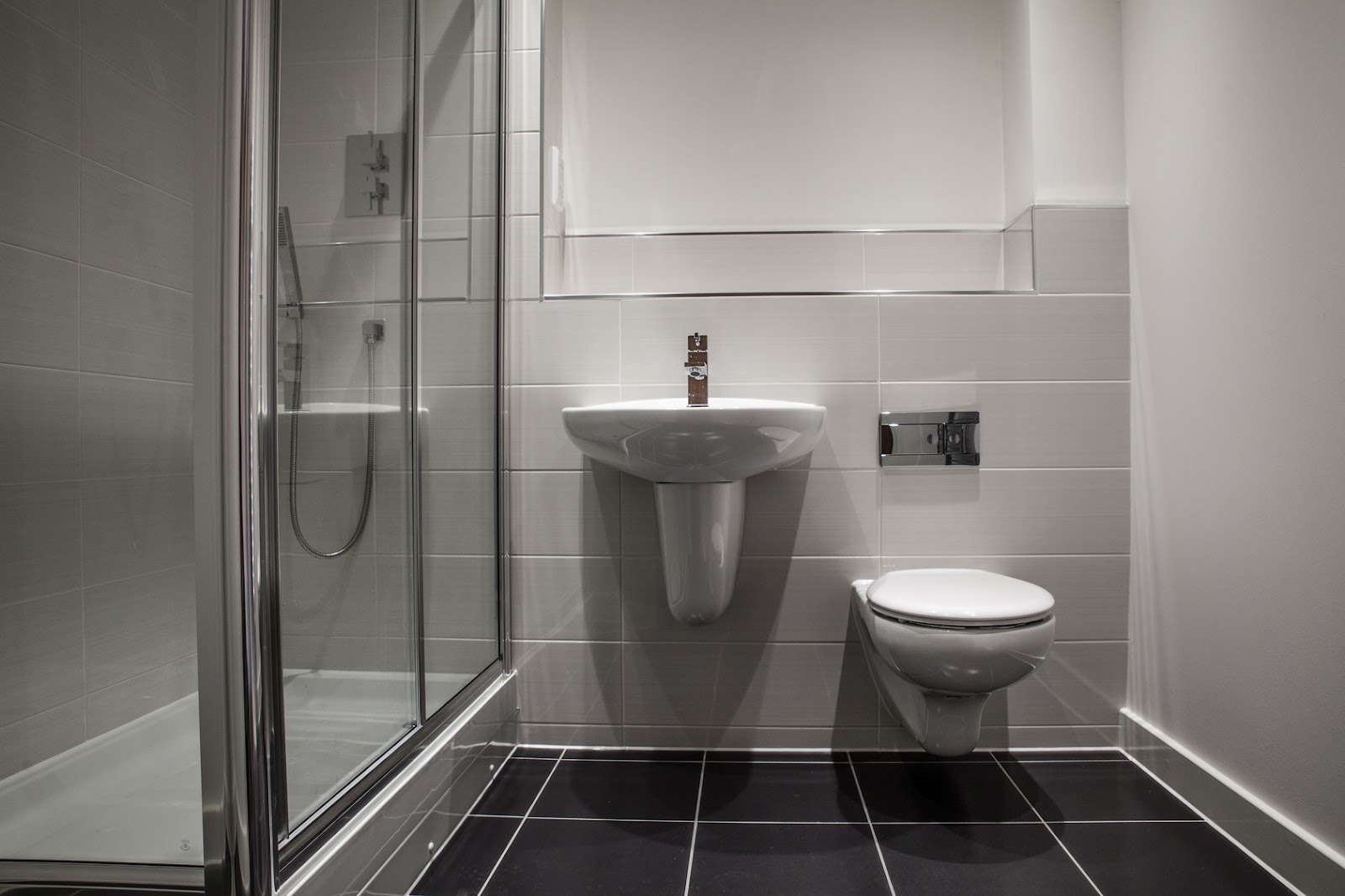 A compact en-suite with a wall-hung basin and WC, concealed cistern and enclosed shower over a dark tiled floor.