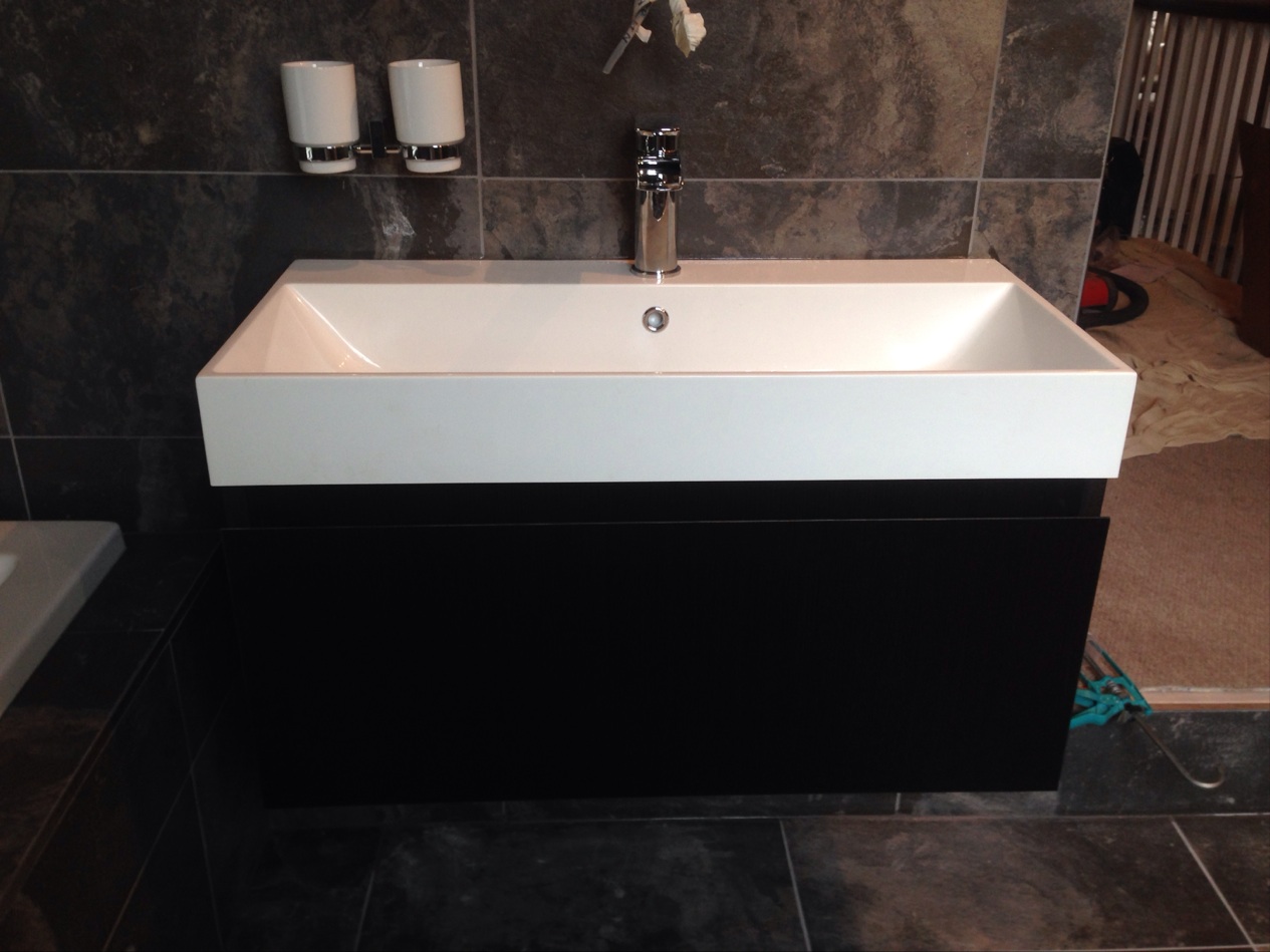 A wide countertop basin on a black wall-hung vanity unit, set against slate wall tiles.